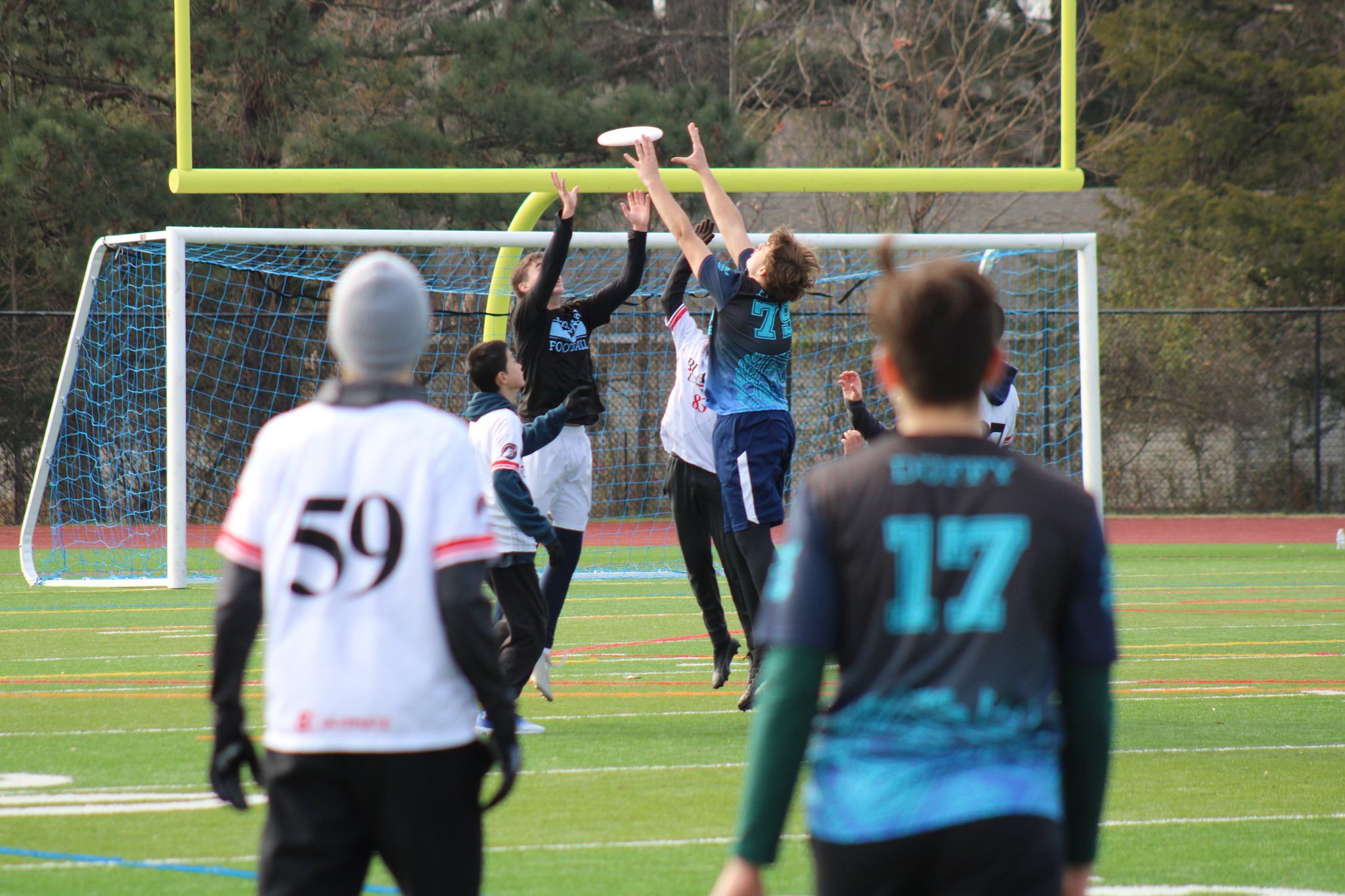 Players leap for the disc in front of the goal at a Poets game